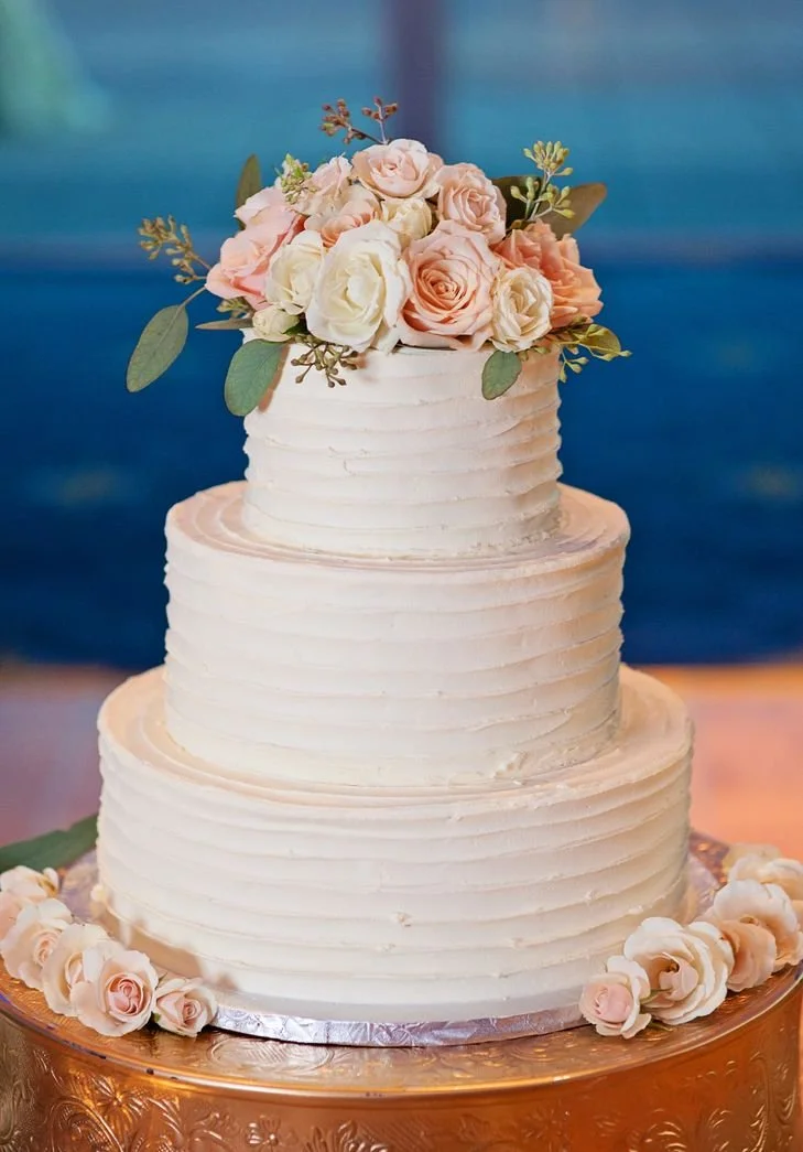 Horizontal Troweled Three Tier Stacked Wedding Cake with No Borders Fresh Rose Pom Arrangement with Fresh Roses Surrounding the Silver Bottom Board