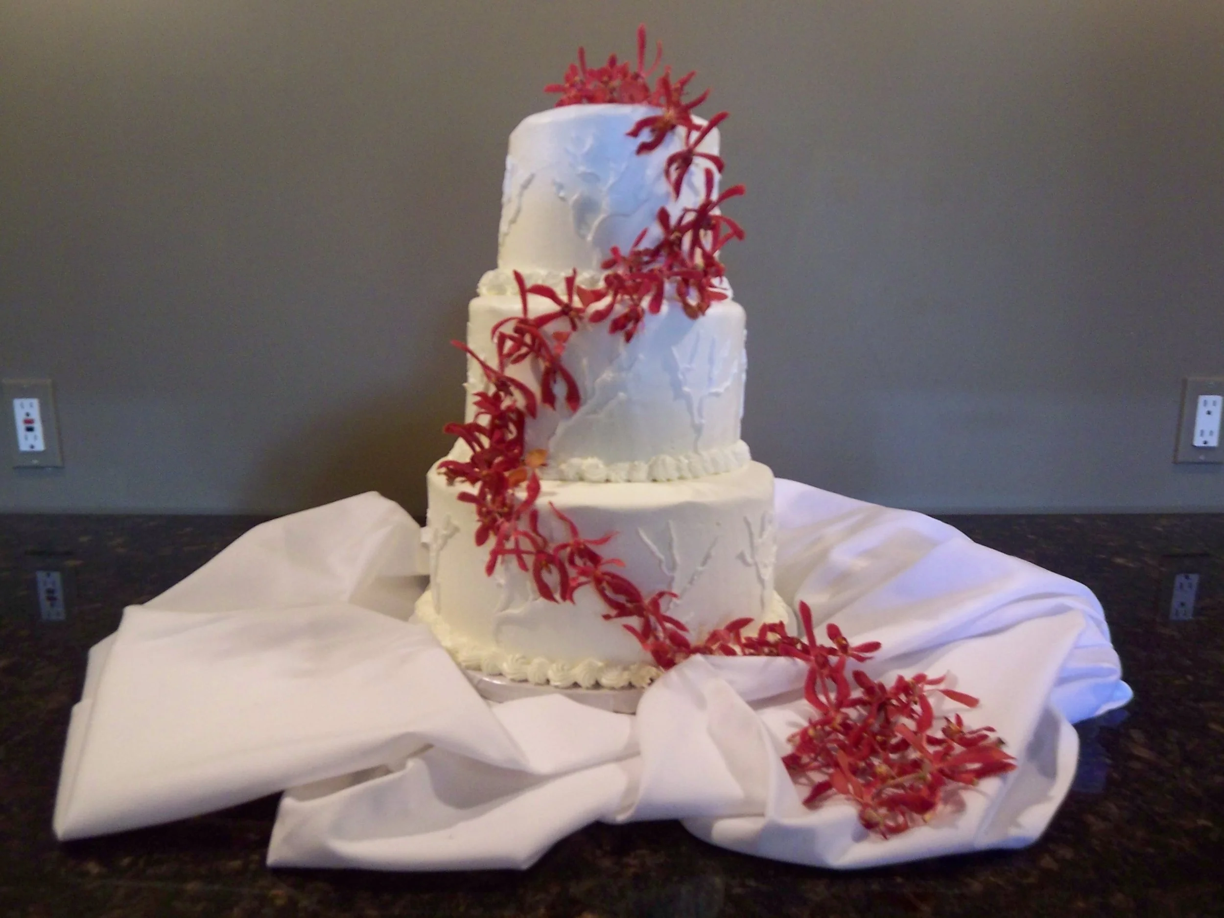 Ocean Inspired Wedding Cake Sitting on Bunched White Linen Three Stacked Tiers with Cascading Fresh Spider Orchids From Top to on Linen