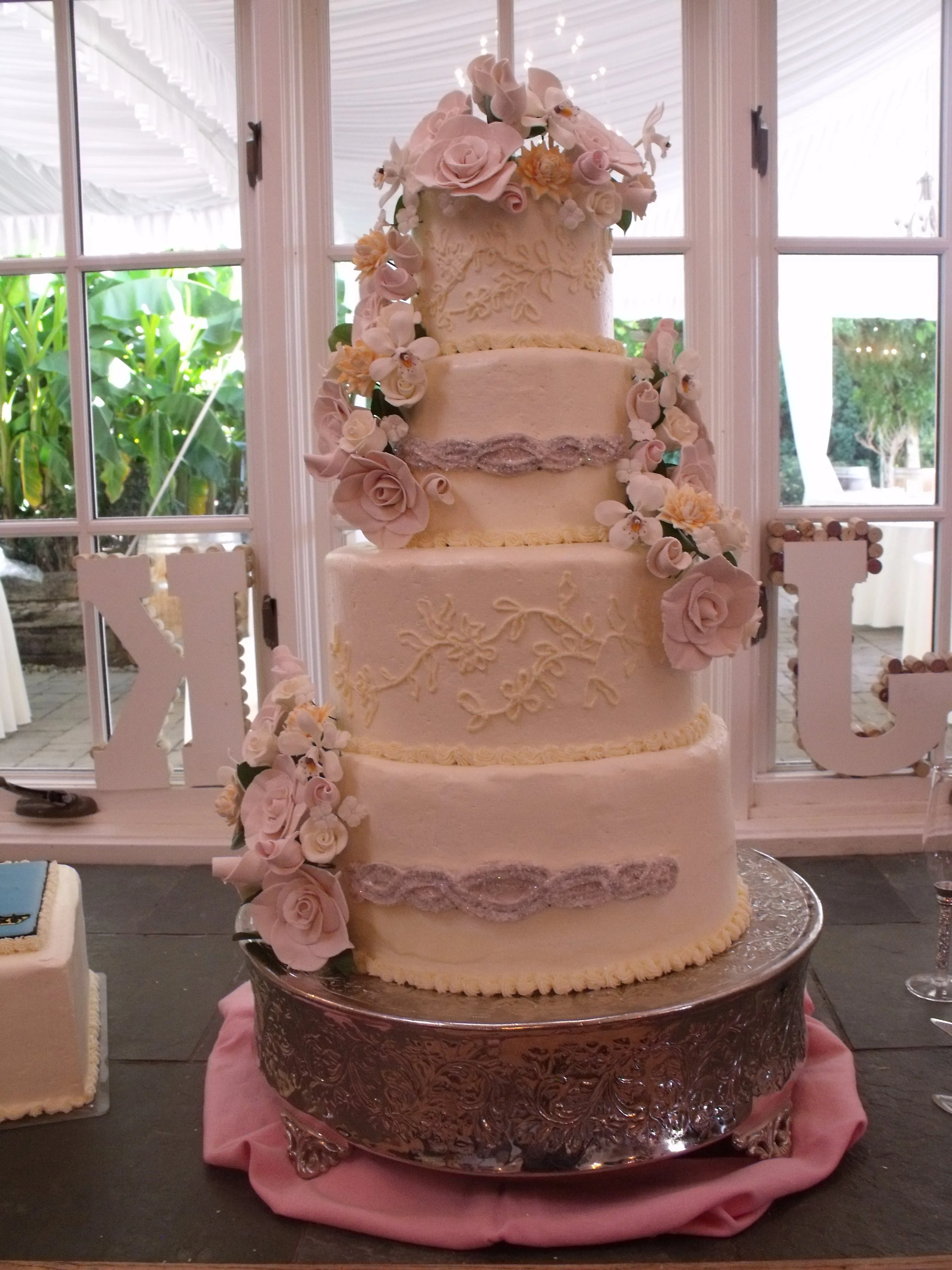 Wedding Cake Four tier stacked Buttercream Frosted round cakes silver cake stand slightly rounded cake edge Fondant crystal sugar Encrusted Creation matching brides dress applique piped lace design on Cake Sides sugar porcelain gardenias roses orchid
