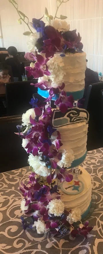 Three Tier Crystal Pillar Separated Wedding Cake Buttercream Frosted Ribbon Sides Seahawks and Steelers Sports Enthusiasts' Inspired  Sugar Emblems Cascade Flowing Fresh Hawaiian Floral From Top Down Front of All Cakes