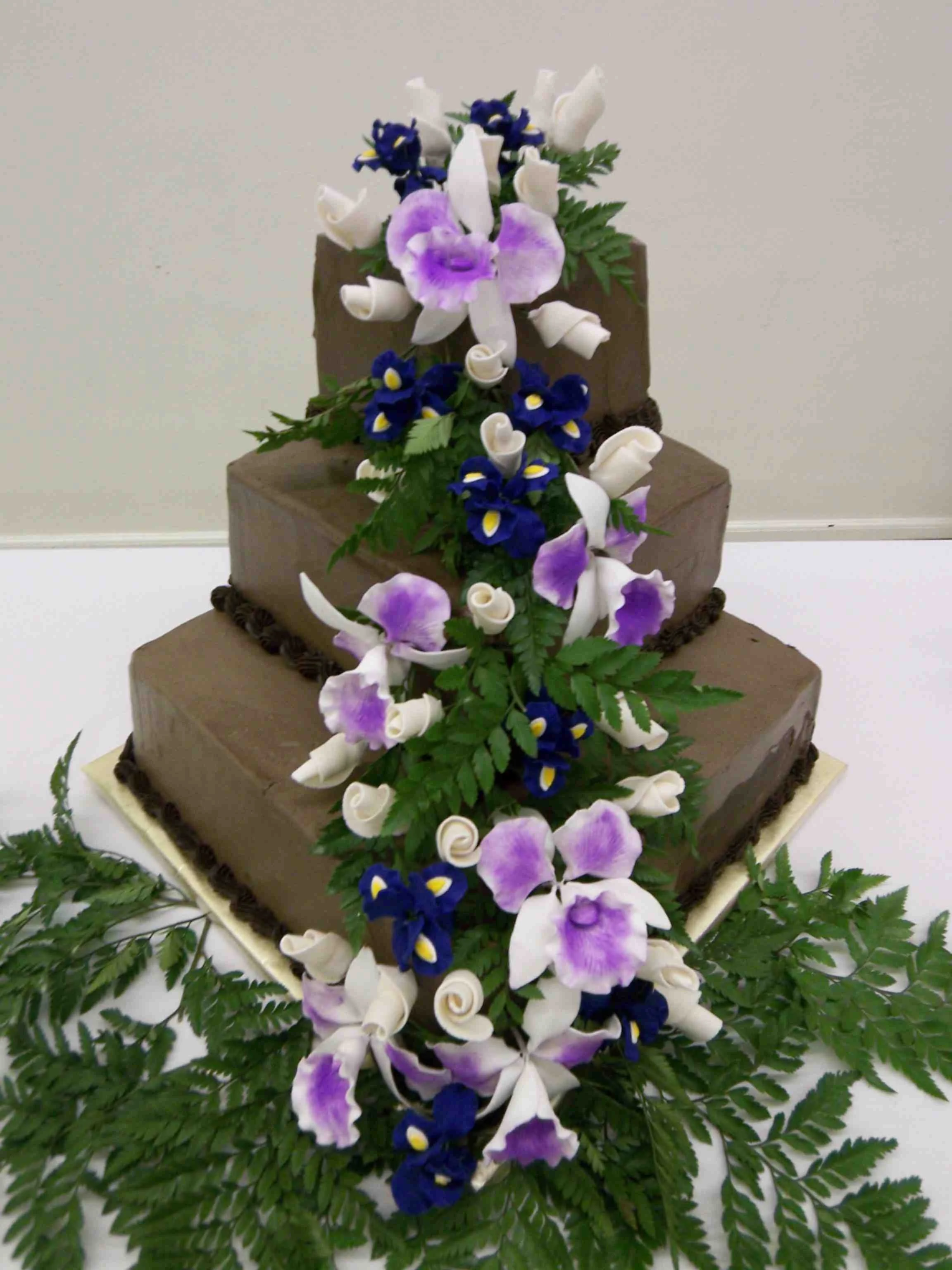 Wedding Cake in Dark Chocolate French Buttercream Backset Stacked Alignment to Give Appearance of Greater Size Definition Between Tiers  Sugar Porcelain Waterfall Orchids Rosebuds Blue Iris Fresh Greens