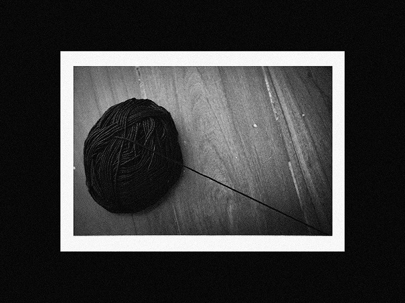 A ball of black yarn with a long strand extending from it, placed on a wooden surface.
