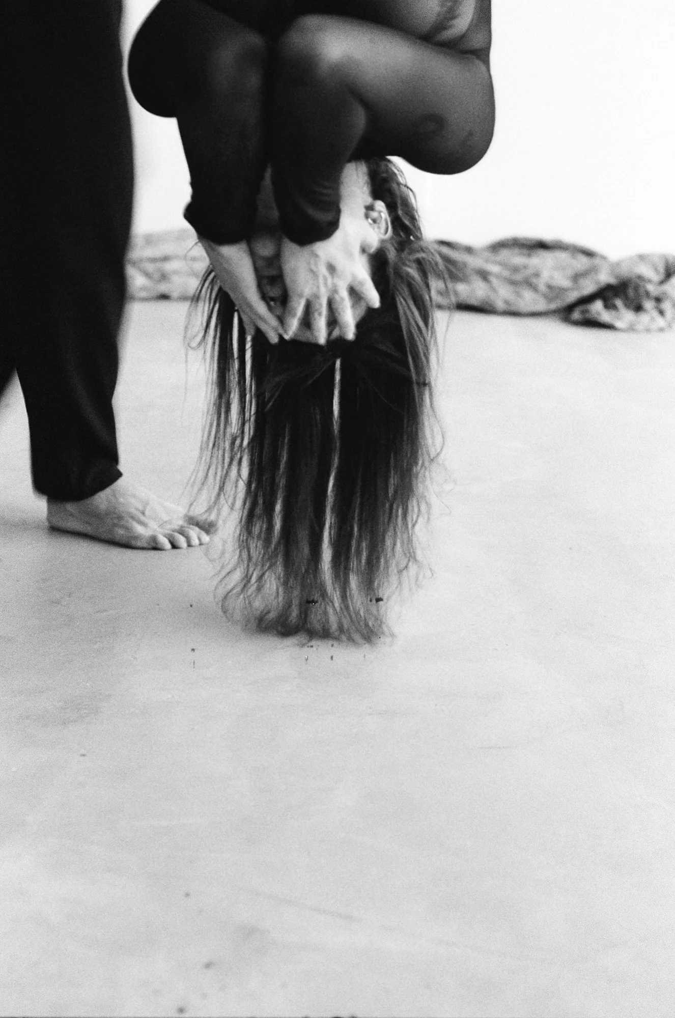 Person performing a headstand in a yoga pose on the floor, with their hair hanging downward and their hands supporting their head.