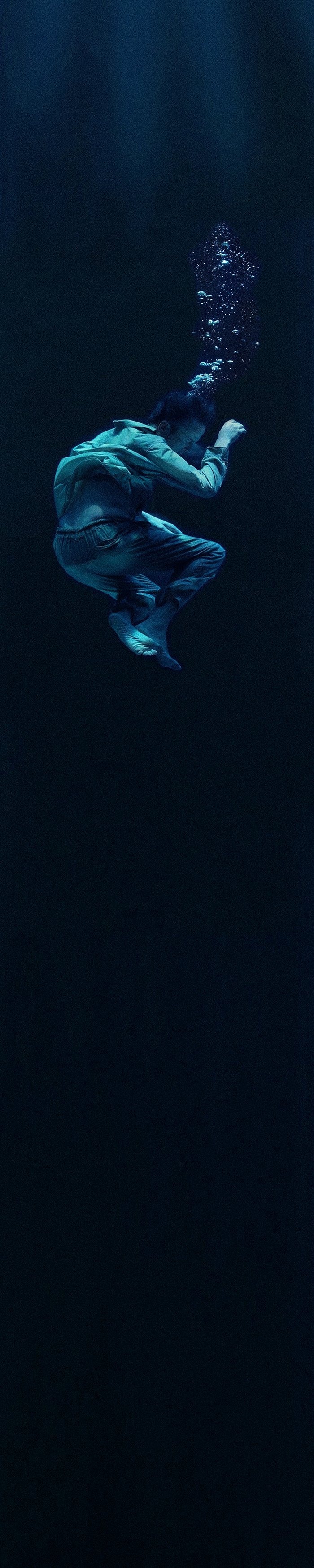 Child in a hoodie and jeans floating underwater, with bubbles rising above.