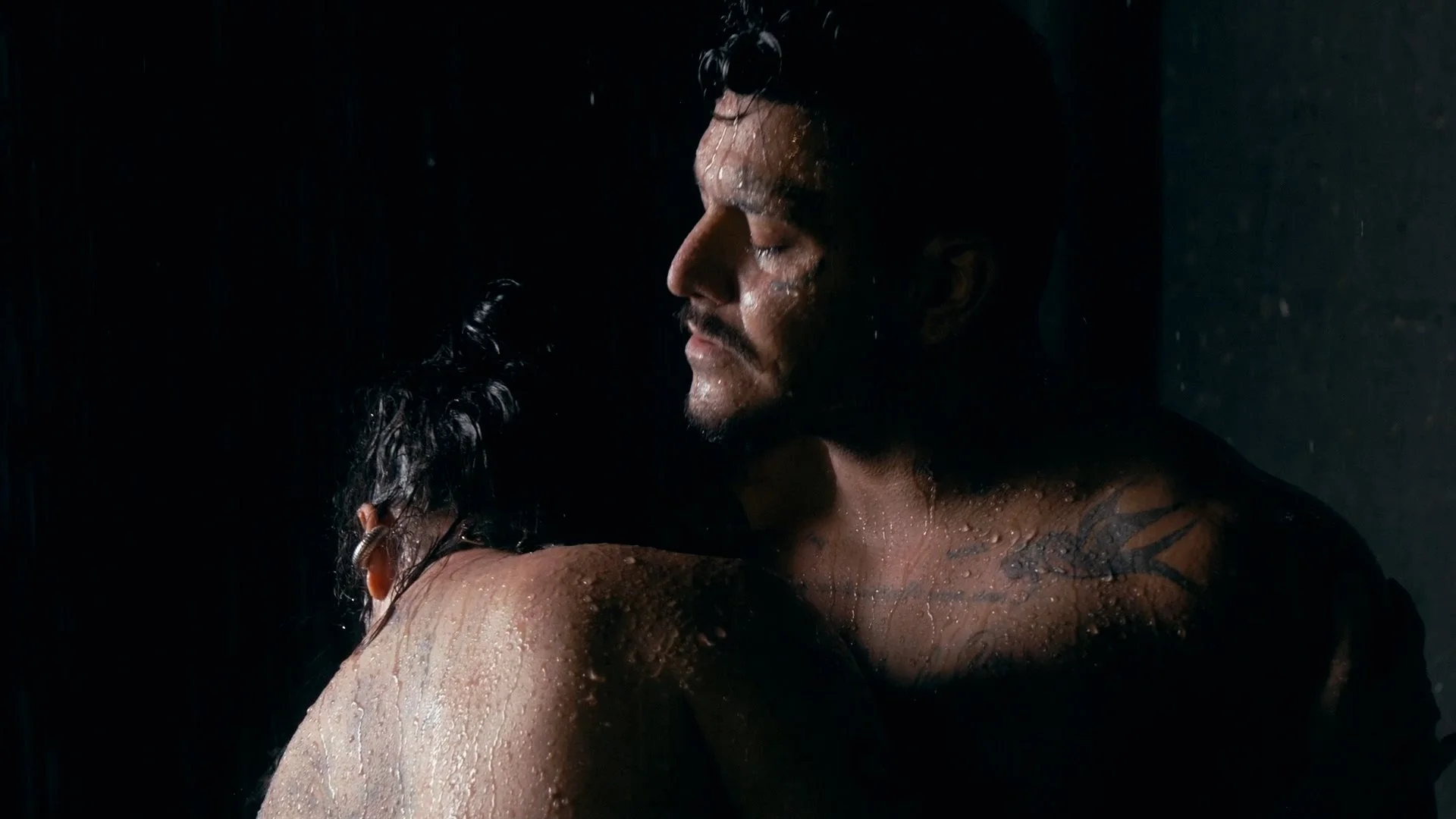 A man and woman in a close, intimate embrace under water, with water droplets on their skin, dark background, somber mood.