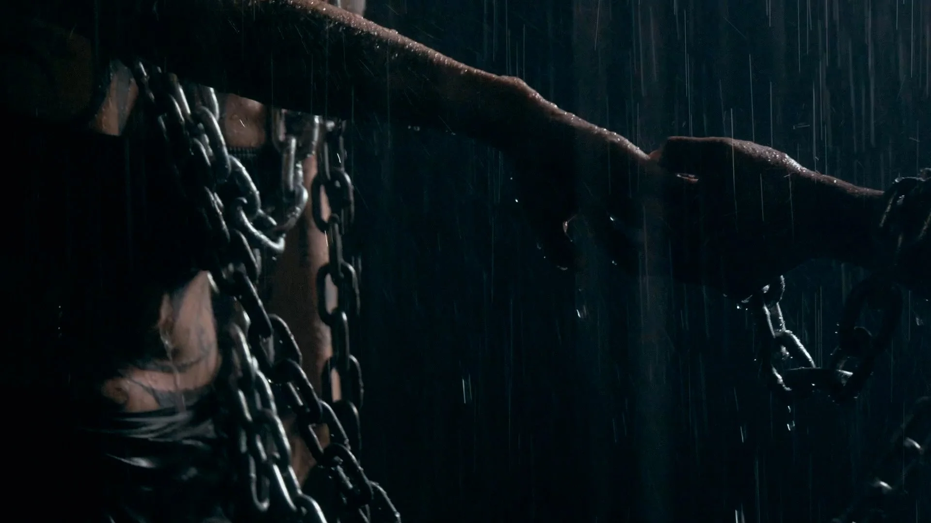 A dark scene showing chains hanging from a structure, with a hand gripping a chain and raindrops falling in the background.