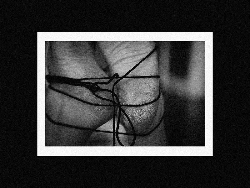 A close-up of fingers with black thread tied around them, forming a knot in the center, in black and white.