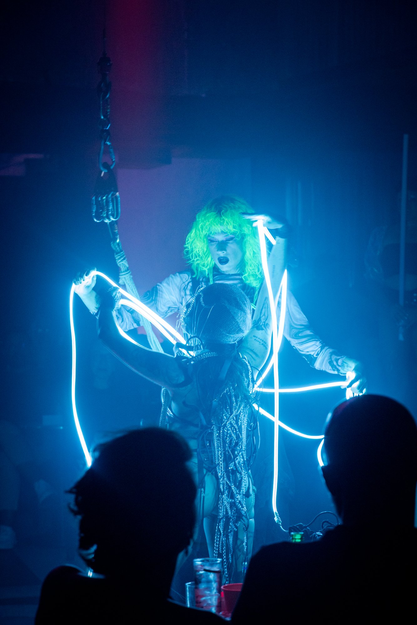 Performer with neon lights and bright green hair on stage at a concert or performance.
