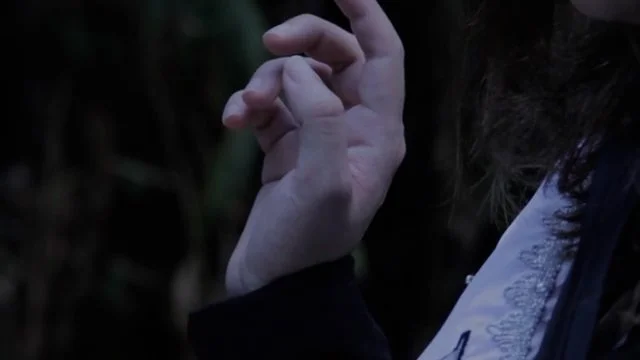 Close-up of a person's hand and part of their face, with the hand slightly raised, in a dark outdoor setting.