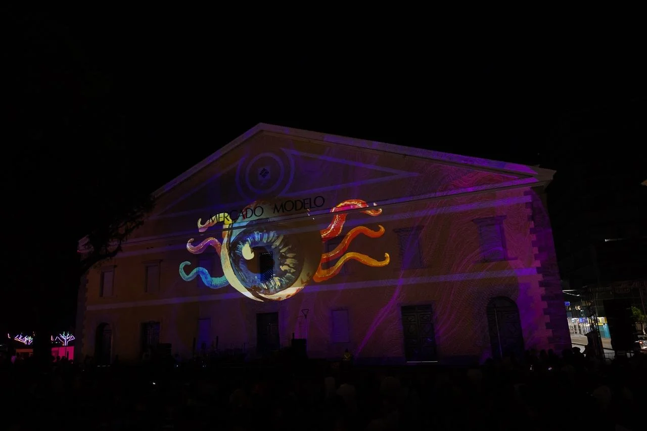 Nighttime projection of an eye with tentacles on a building face with text 'LIMBERADO MODELO' nearby.