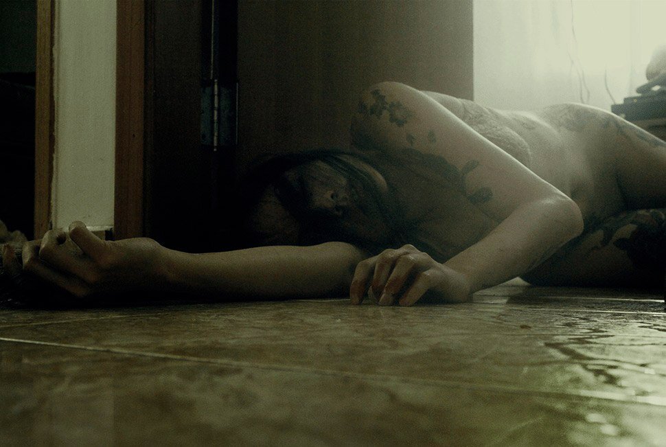 Person lying on the floor with their arm stretched out, in a dimly lit room.