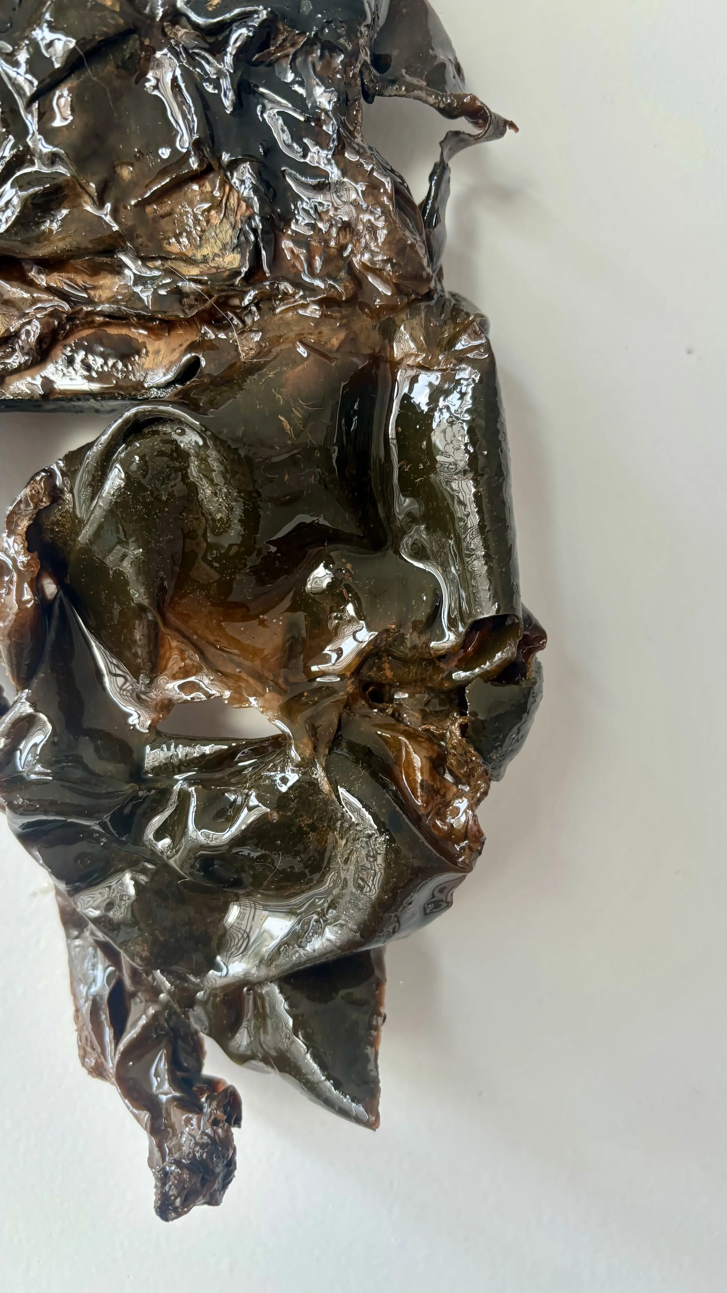 A crumpled and shiny piece of dark brown or black foil or plastic material on a plain white surface.