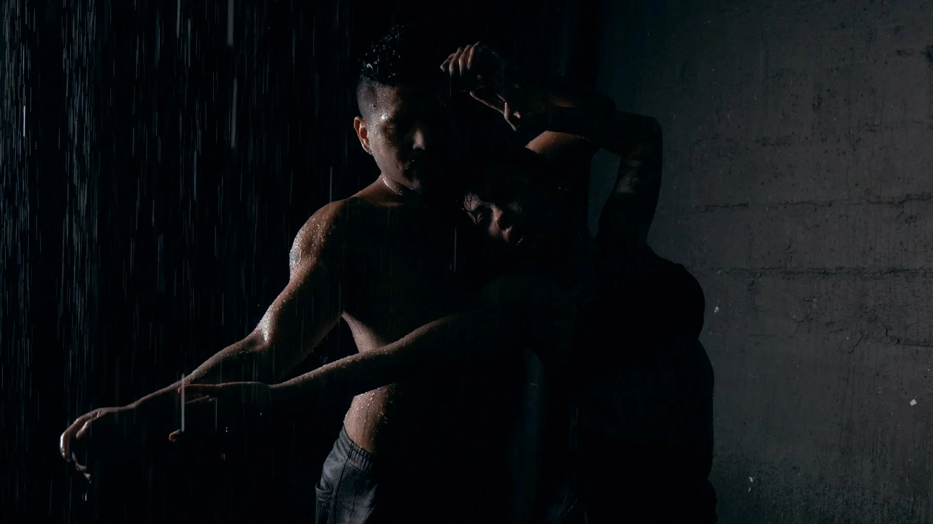 A man and woman embracing in the rain at night, with a dark background and minimal lighting highlighting their outlines.