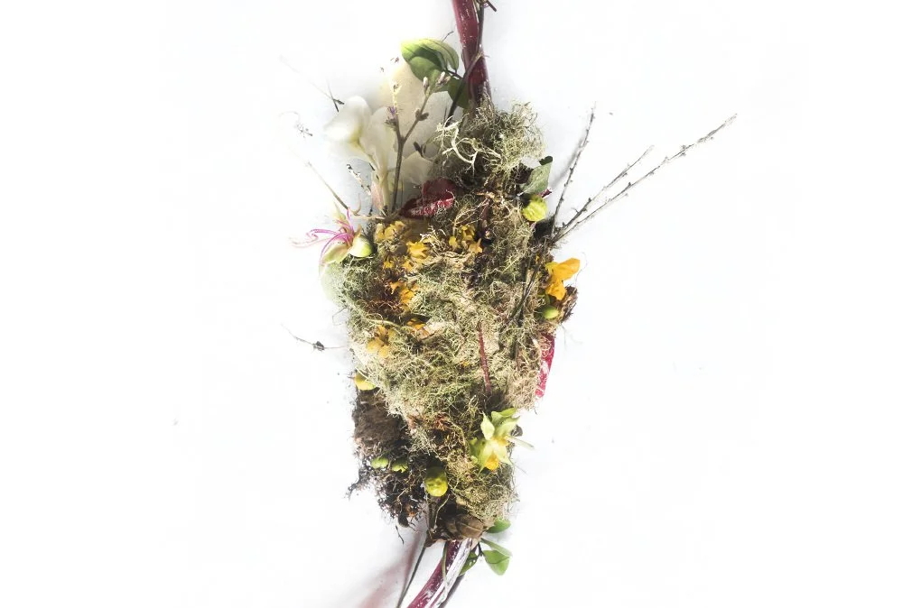A floral arrangement with various flowers, moss, and twigs arranged vertically against a white background.