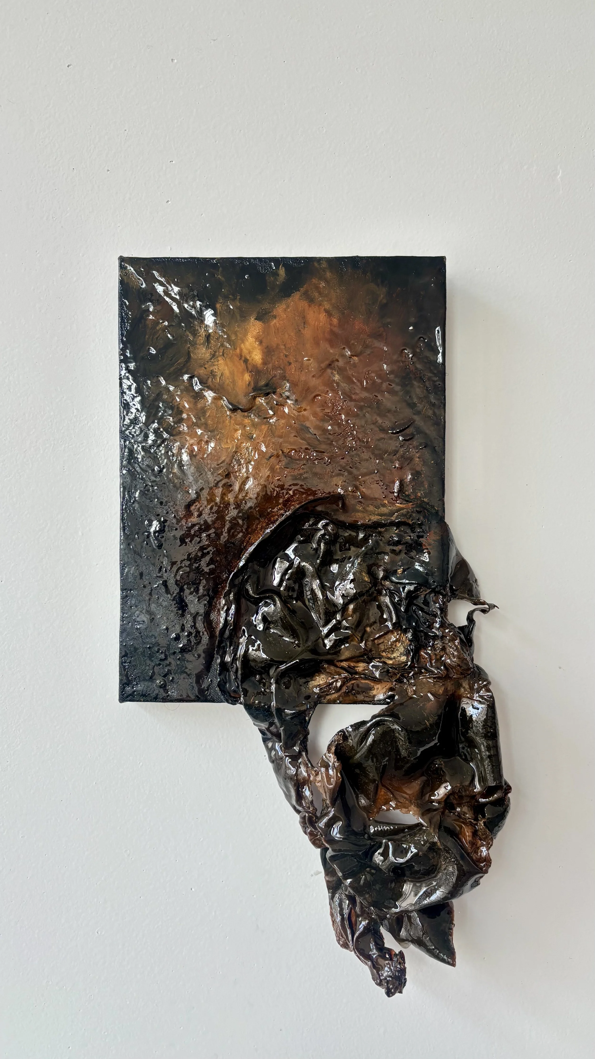 Abstract mixed media art piece with textured, dark, and metallic elements mounted on a white wall.