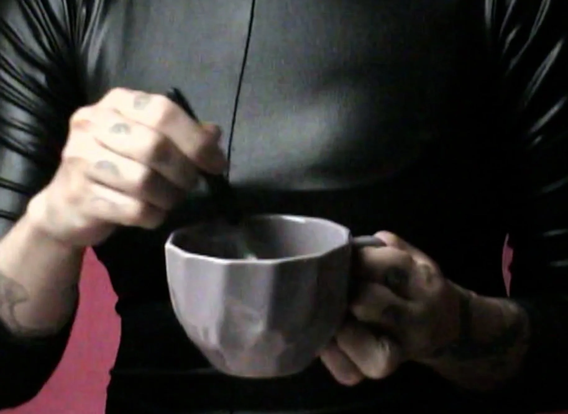 Person wearing black shirt holding a white mug and stirring a dark-colored liquid with a spoon.