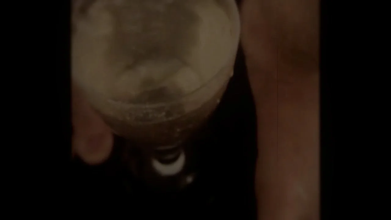 A person holding a glass with a layered drink, seen from above, with a dark background.