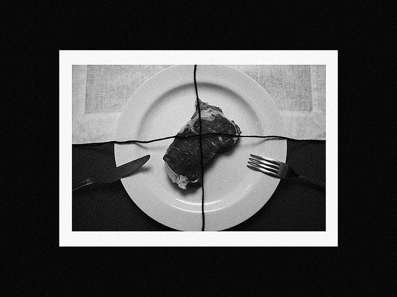 Black and white photo of a plate with a single piece of meat, surrounded by a knife on the left and a fork on the right, with paper under the plate, divided into four sections by black lines.