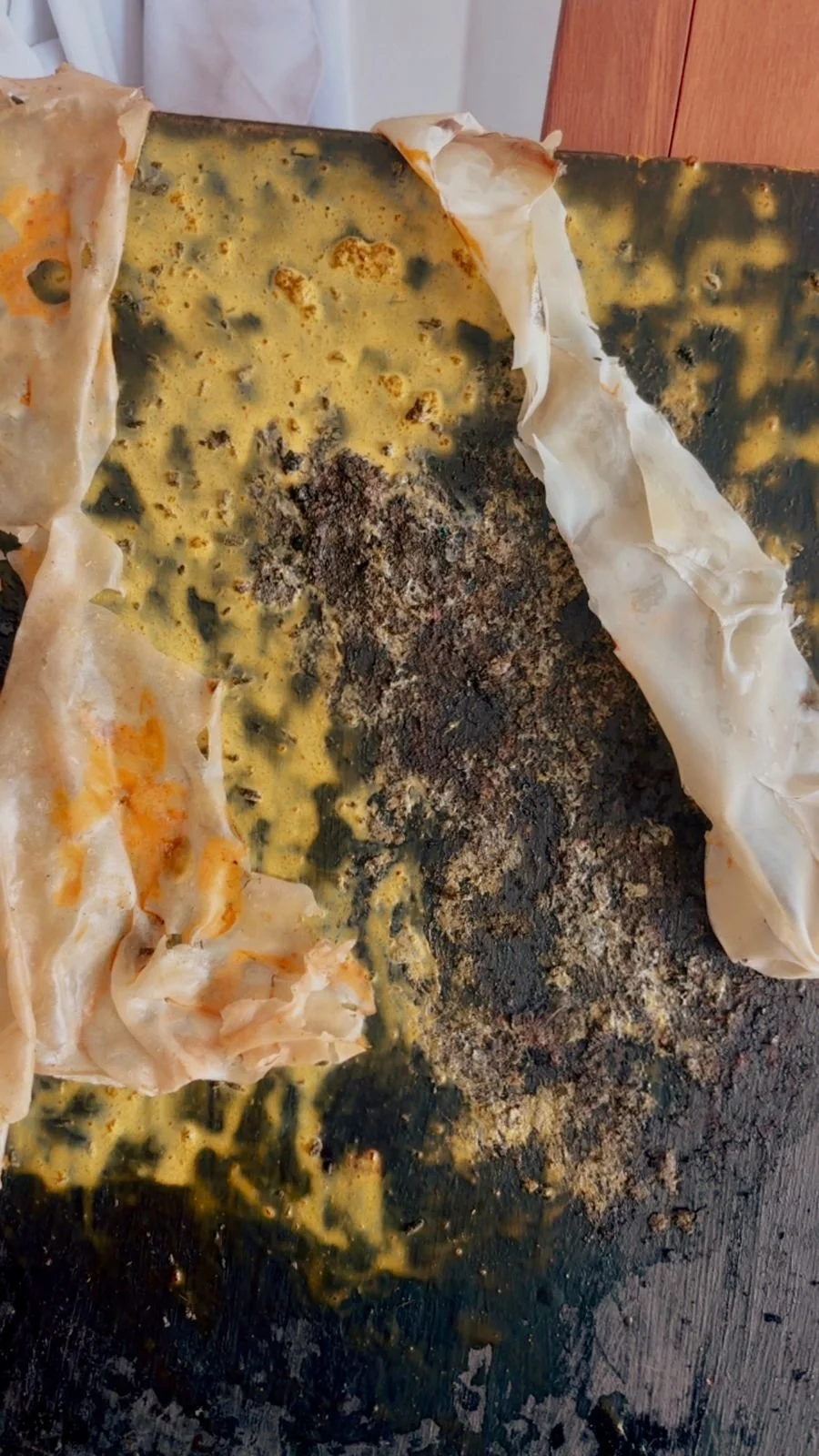 A burnt and greasy blackened baking sheet with crumpled parchment paper and remnants of a cooked or burnt food item.