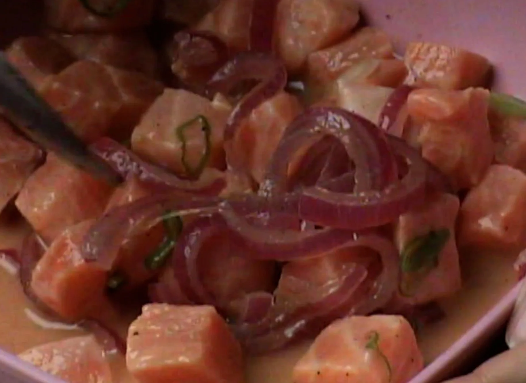Close-up of a dish with cubed pink meat, sliced red onions, and green herbs in a creamy sauce.