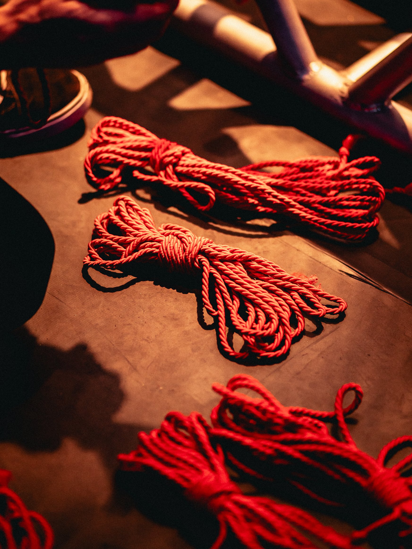 Red climbing rope coiled on a dark surface with a skateboard and shoes in the background.