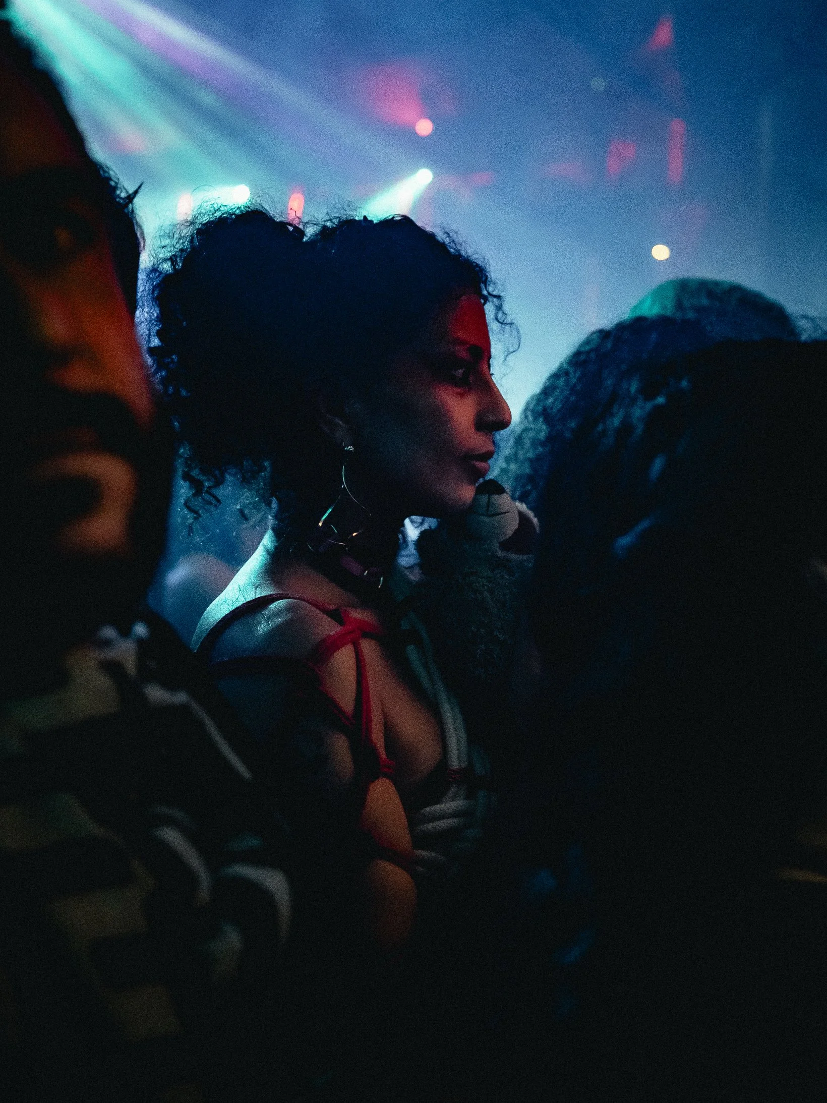 A woman with curly hair on stage at a concert, holding a microphone, with colorful stage lights