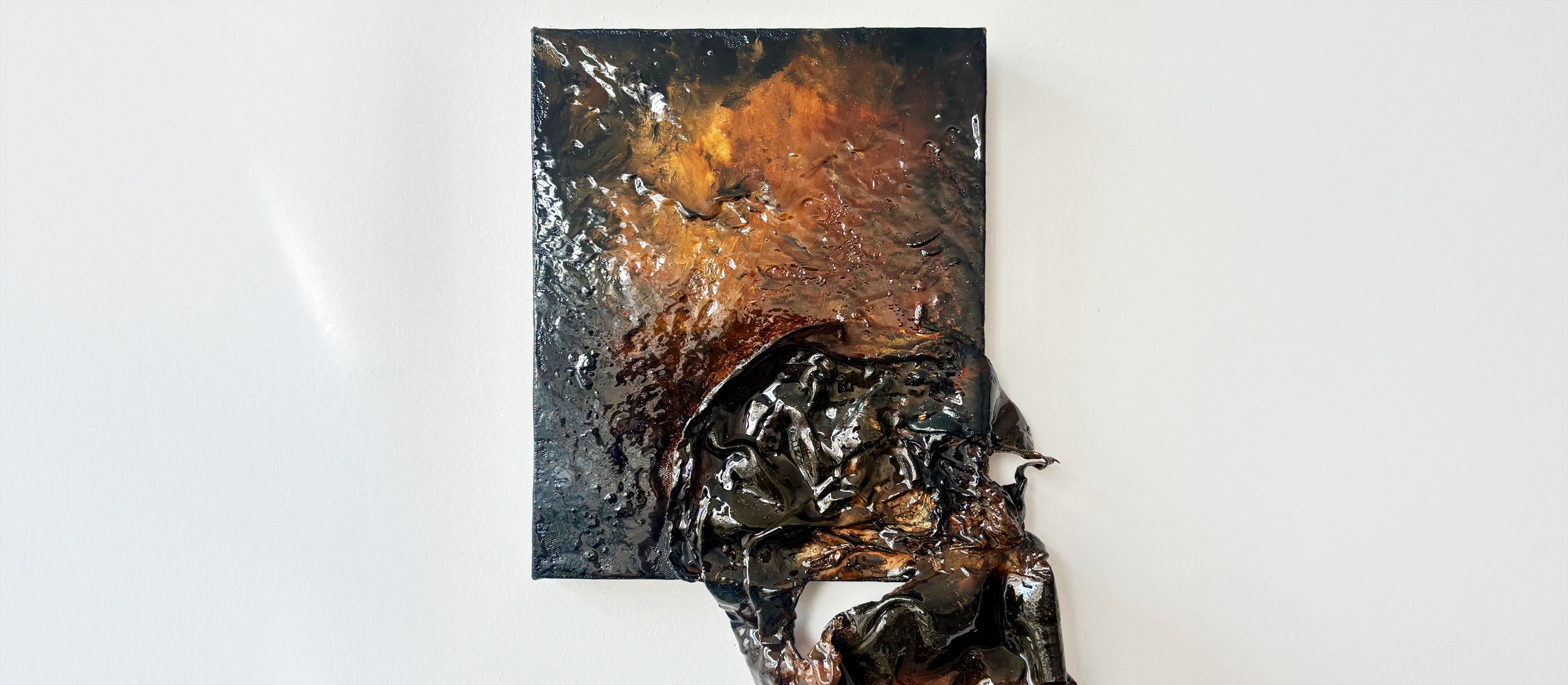 Mixed media abstract art piece with textured black, brown, and copper-colored materials on a white wall.