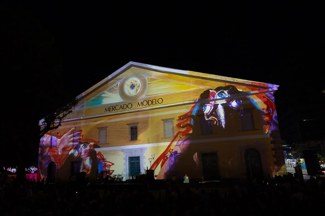 Nighttime projection on a historic building featuring a graphic of a crab, colorful abstract designs, and the words 'Mercado Modelo'.