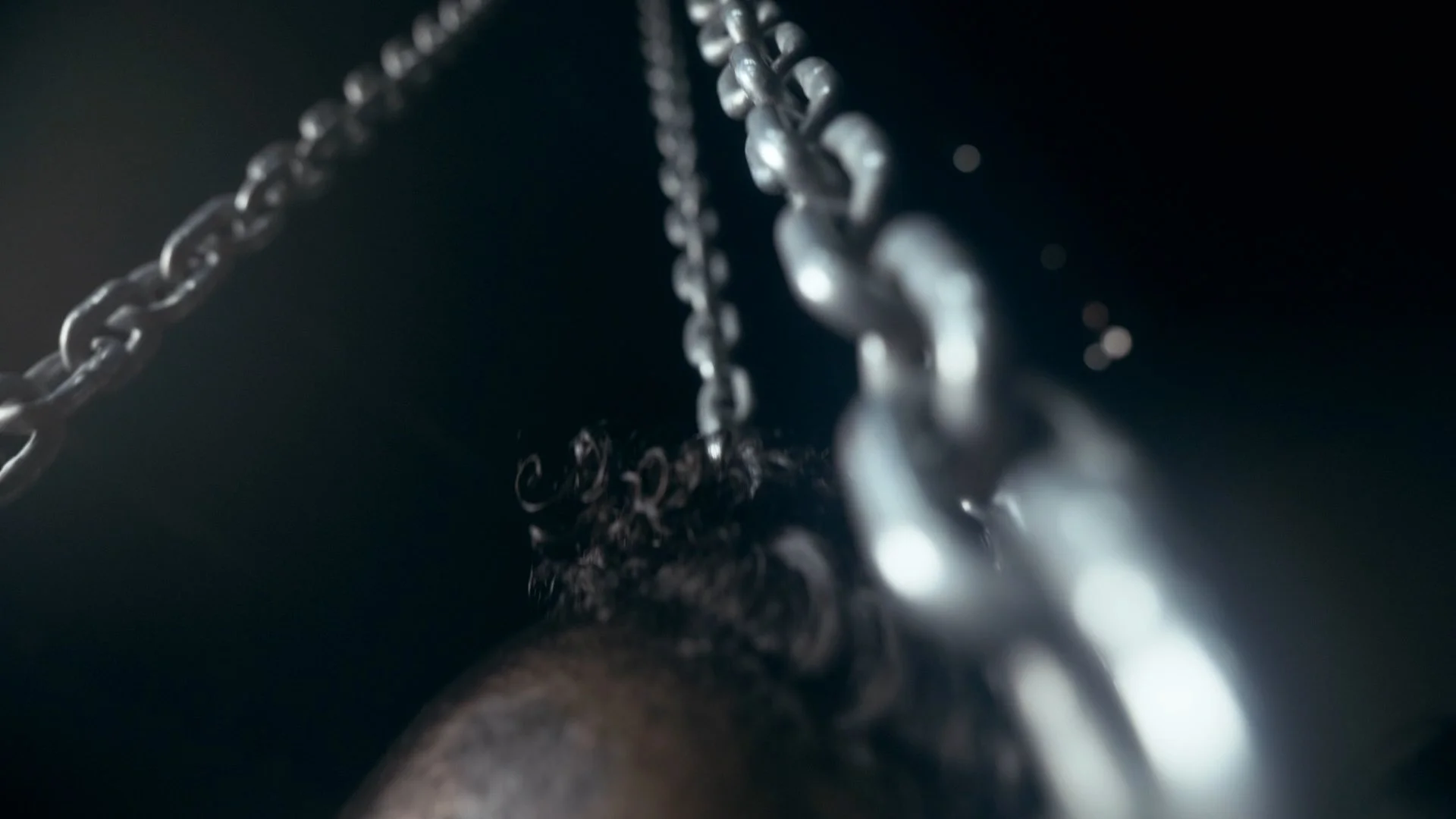 Close-up of chains hanging in darkness with soft light reflecting off the metal links.
