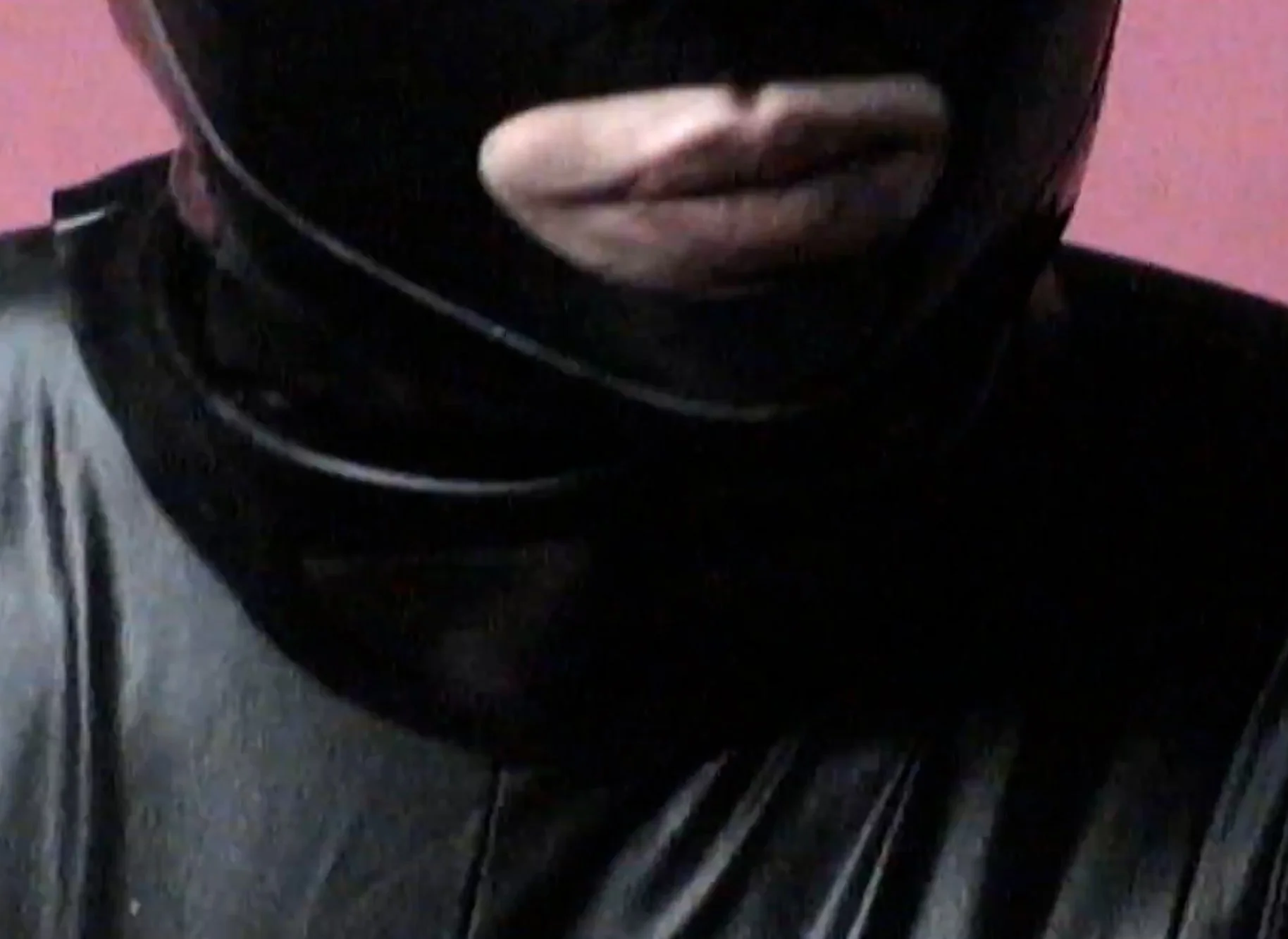 Close-up of a person wearing a black helmet, with visible lips and part of face showing, against a pink background.