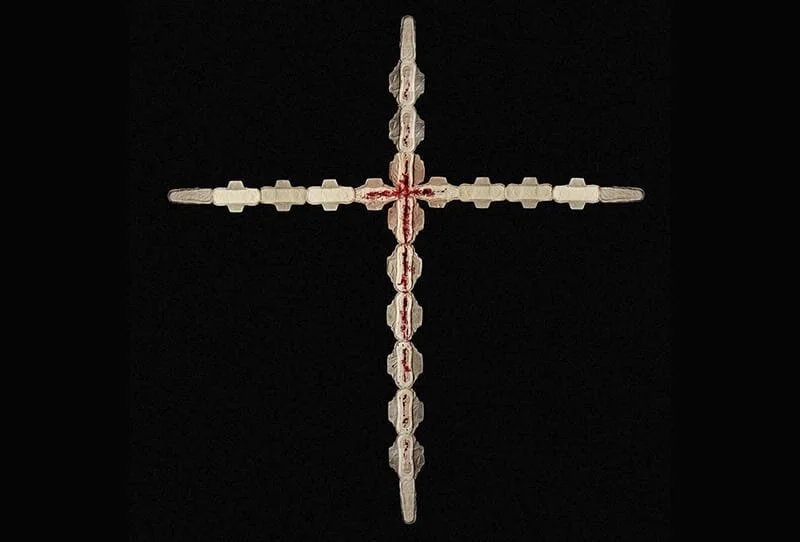 A cross made from stacked white pills with red markings, set against a black background.