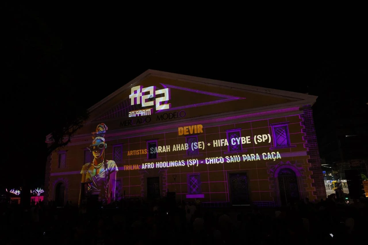 Building with projected colorful light display featuring a woman with sunglasses and text about an event, including artist names and a music trail.