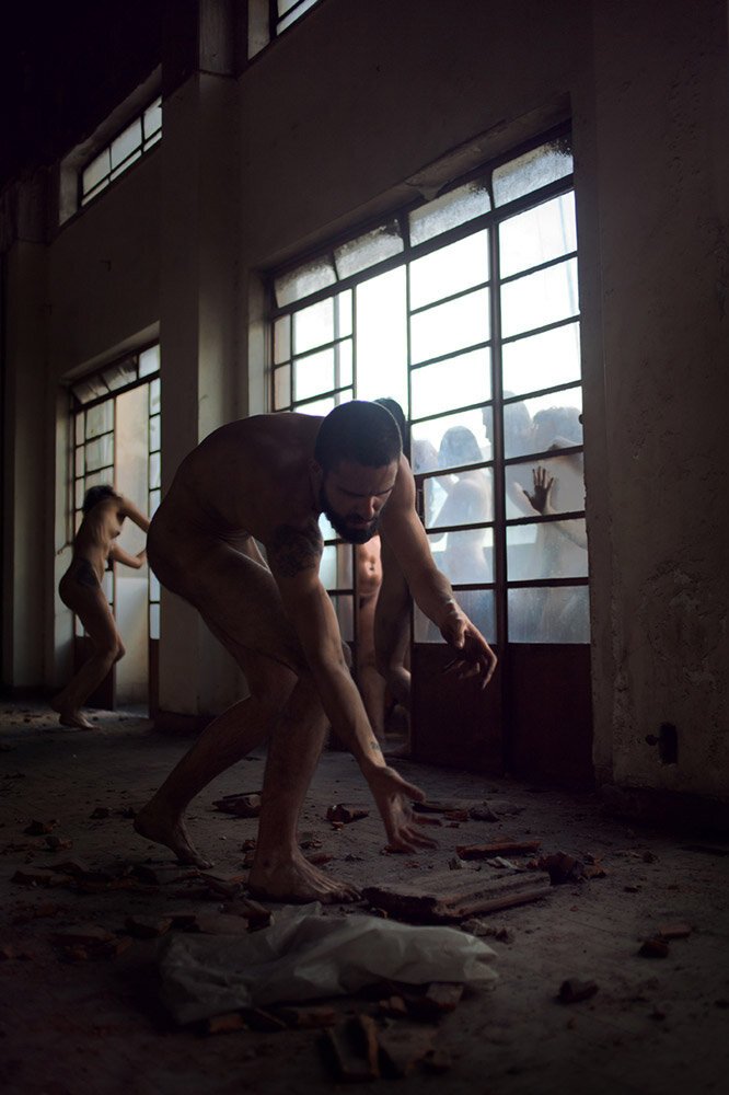 People cleaning broken glass inside a building with large windows, some are outside looking in through the glass.