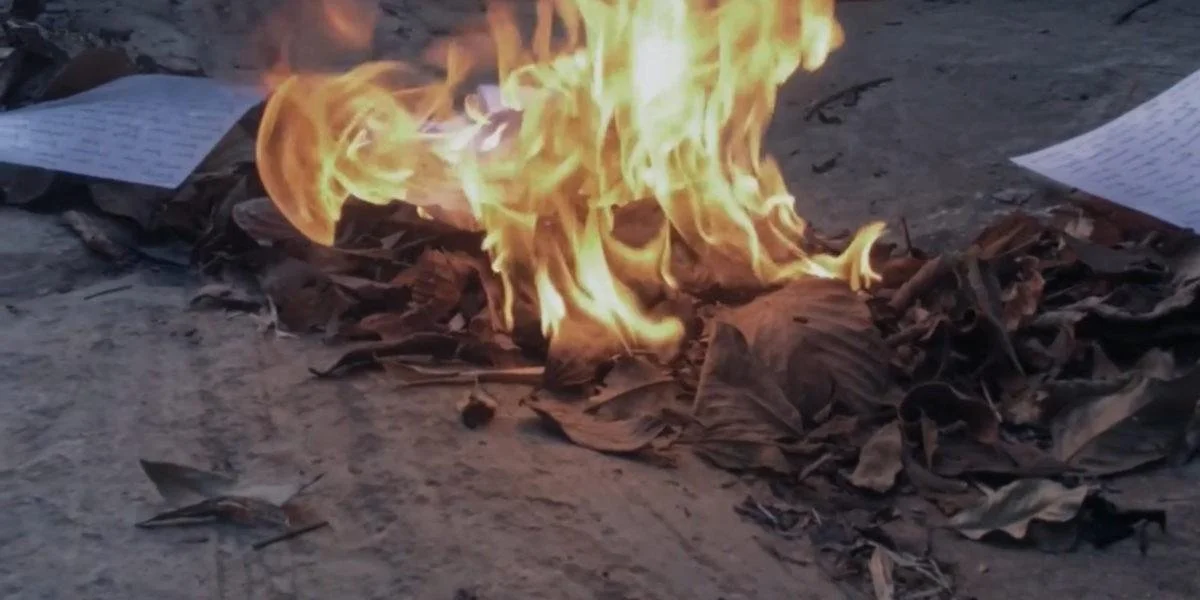 Paper and leaves burning on the ground with flames.