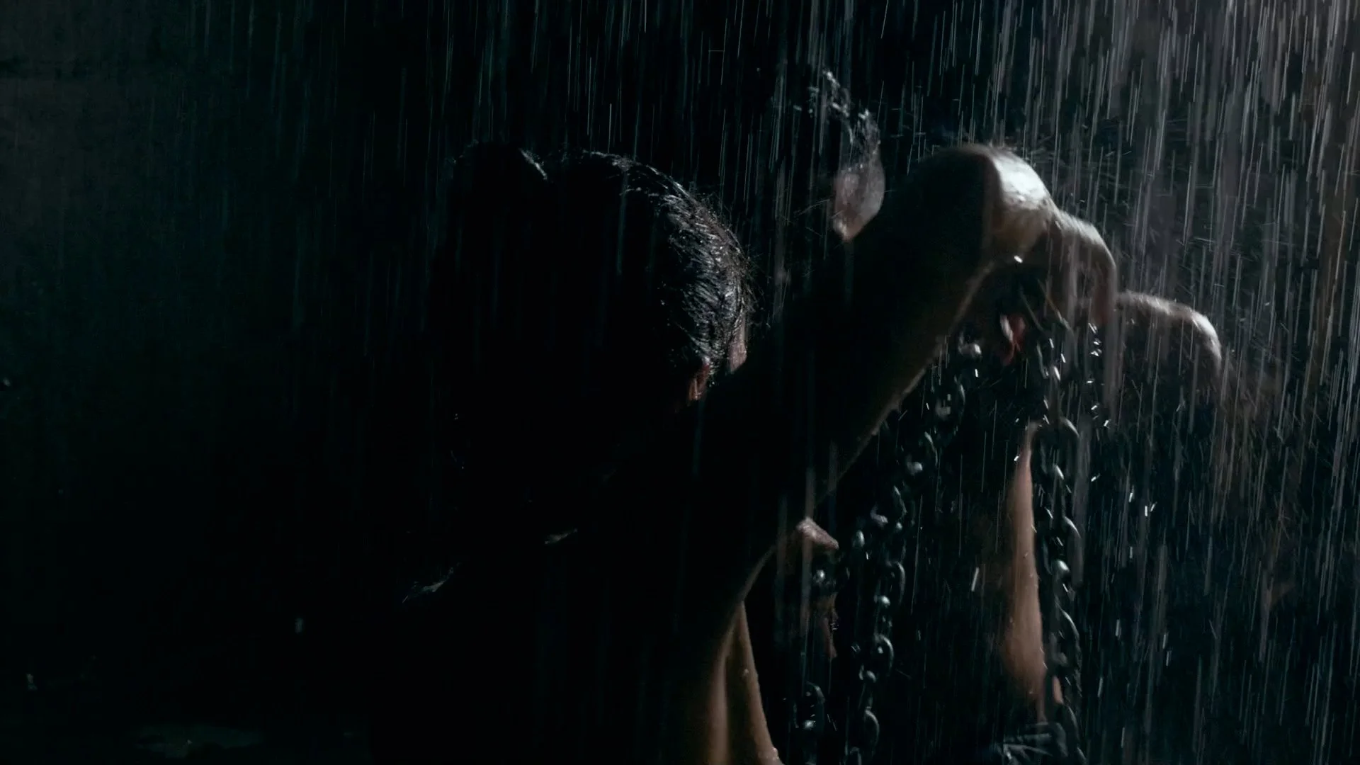 Man with chains around his neck and head, leaning forward in the rain at night.