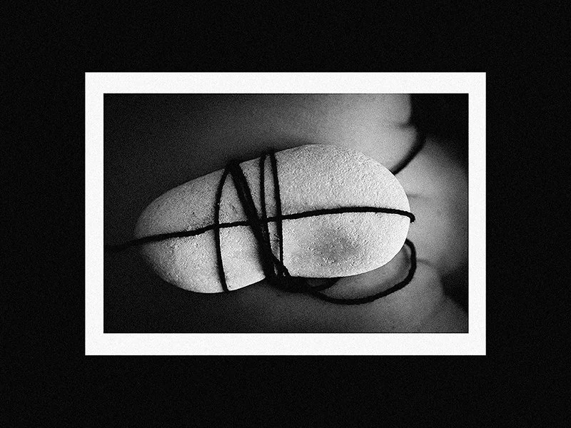 Black and white photo of a capsule-shaped pill tied with black string.