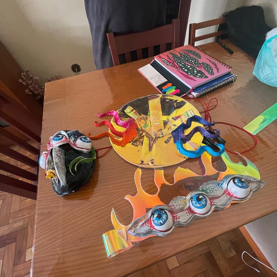 Colorful eye-themed masks, a bright yellow circular stand with multicolored tentacles, and rainbow-colored flame-shaped decorations on a wooden table.