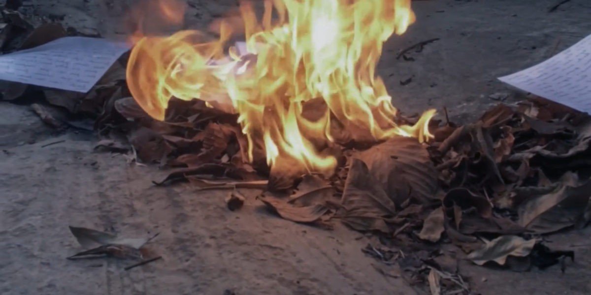 Paper documents burning on the ground with bright flames and ashes.