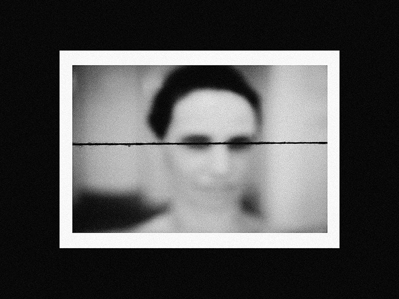 A black and white photograph of a woman's face, partially obscured by a horizontal line across the middle, with a white border against a black background.