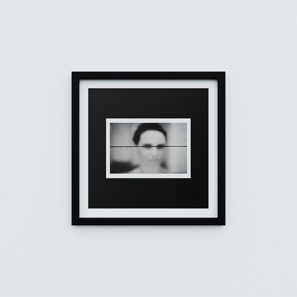 Framed black and white abstract art with a blurred photo of a person's face with glasses, hung on a plain white wall.