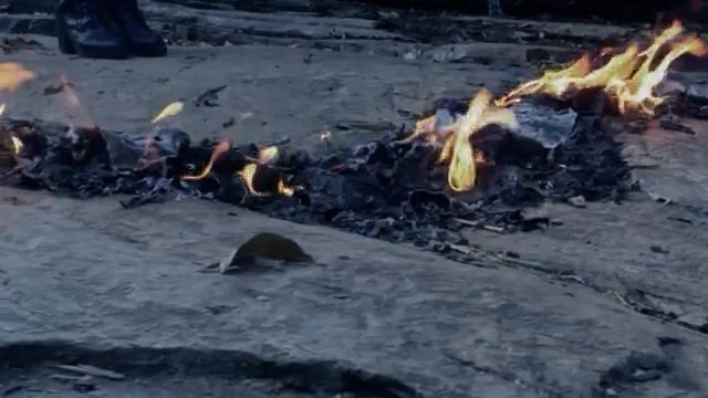 Charcoal and flames from burning wood or debris on a ground surface.