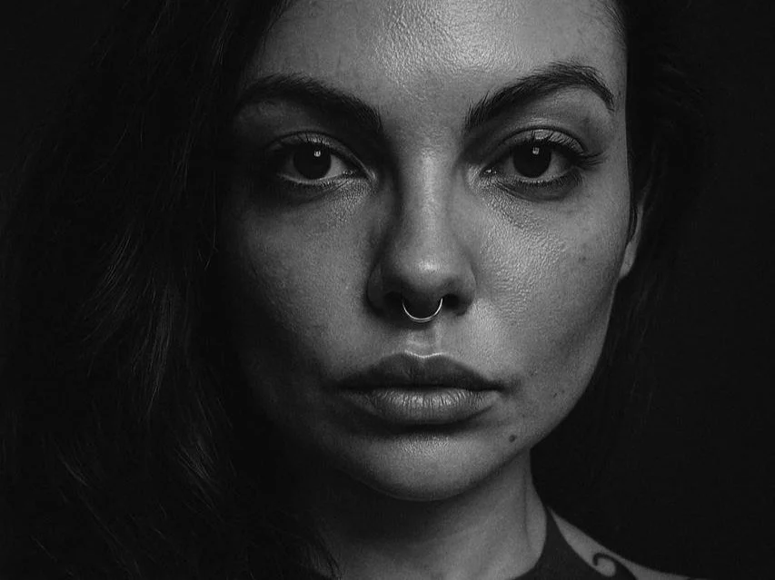 Black and white close-up portrait of a woman with dark hair, septum piercing, and intense gaze.
