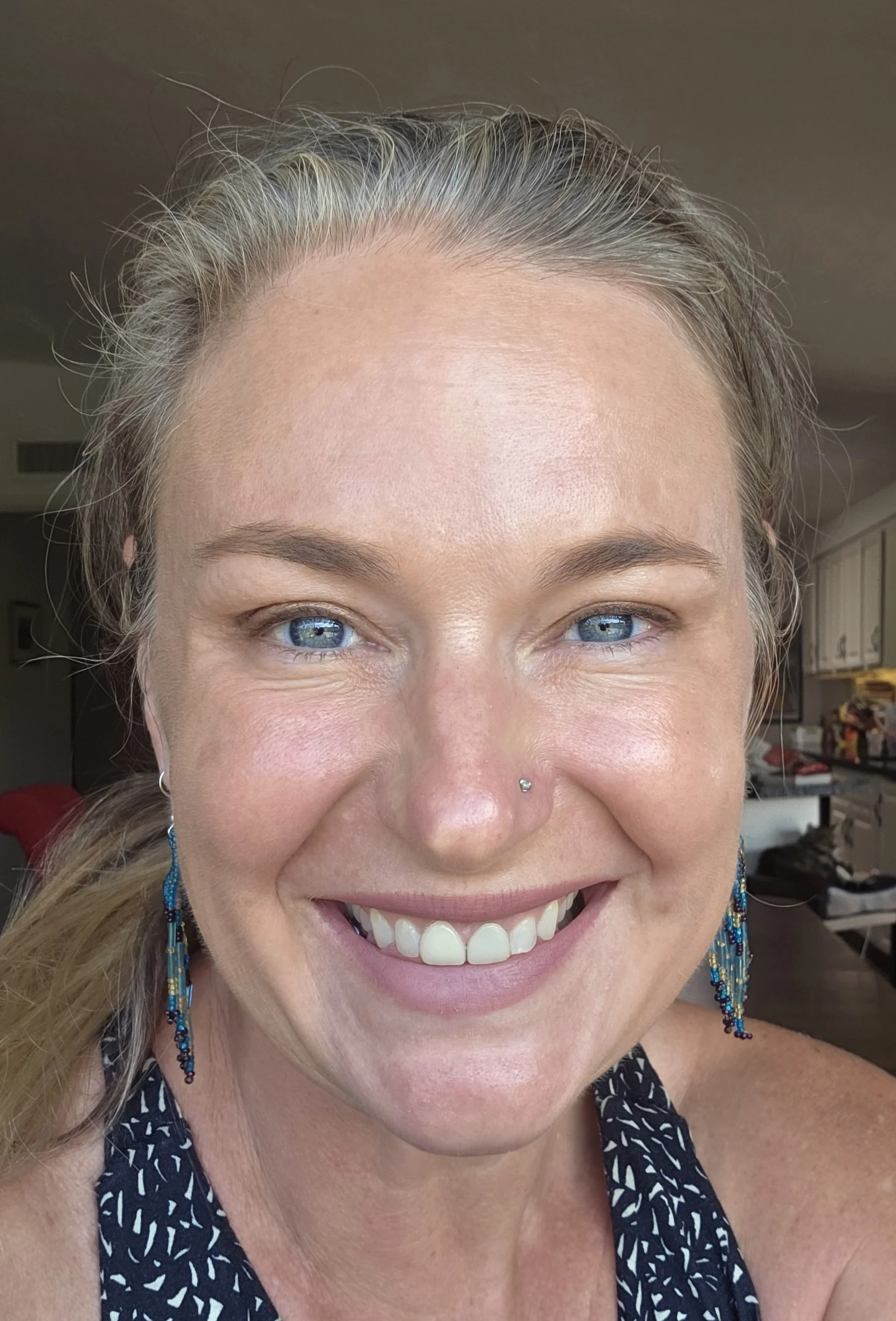 A young woman with painted face smiling outdoors under a blue sky with clouds, mountains, and a fence in the background.