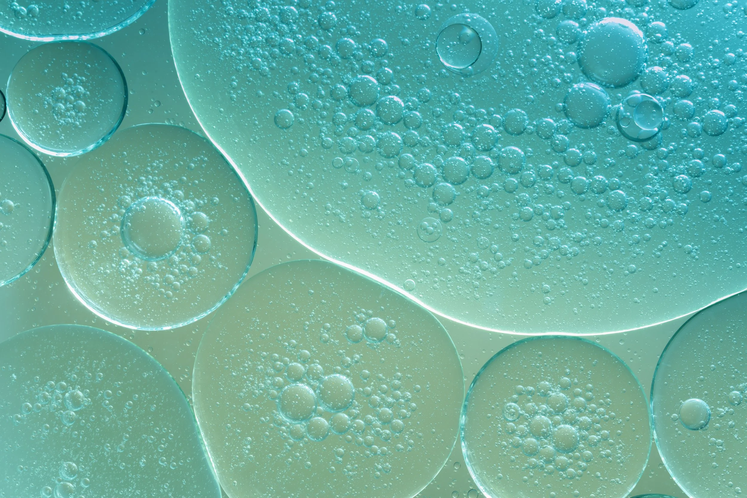 Close-up of oil droplets in water, showing circular shapes and bubbles in shades of blue and green.