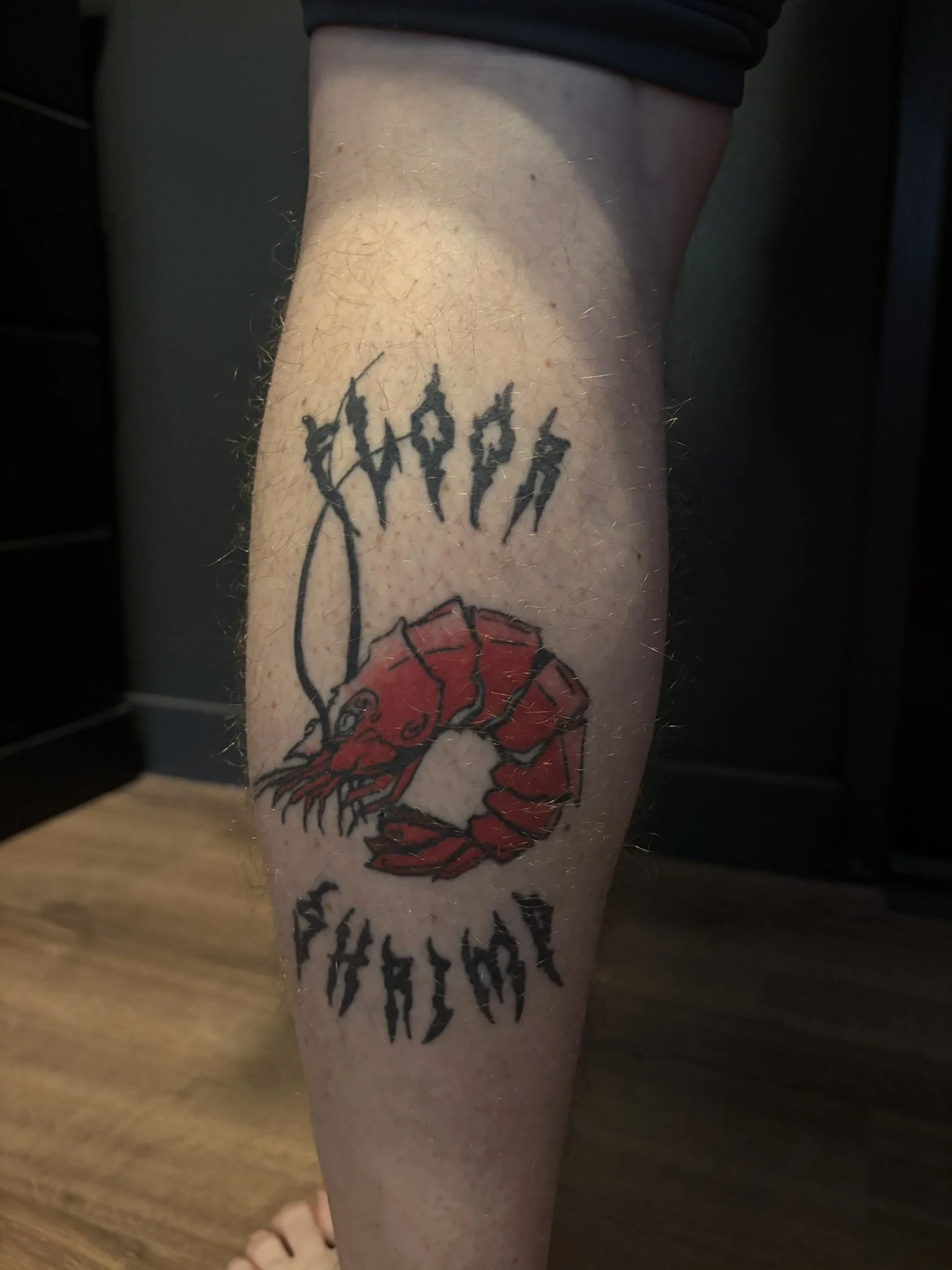  Dark gothic shrimp tattoo in color on calf with text arced on top and bottom 