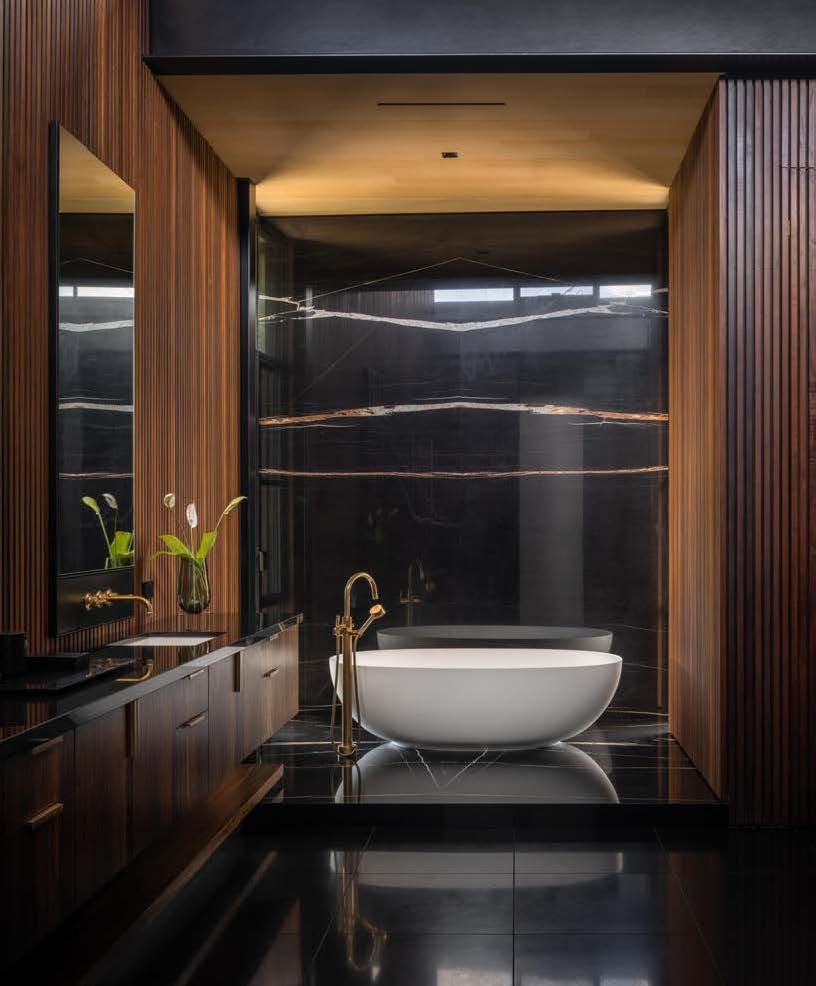 Modern bathroom with a white freestanding bathtub, black marble walls with gold veining, dark wood paneling, and a black tiled floor.