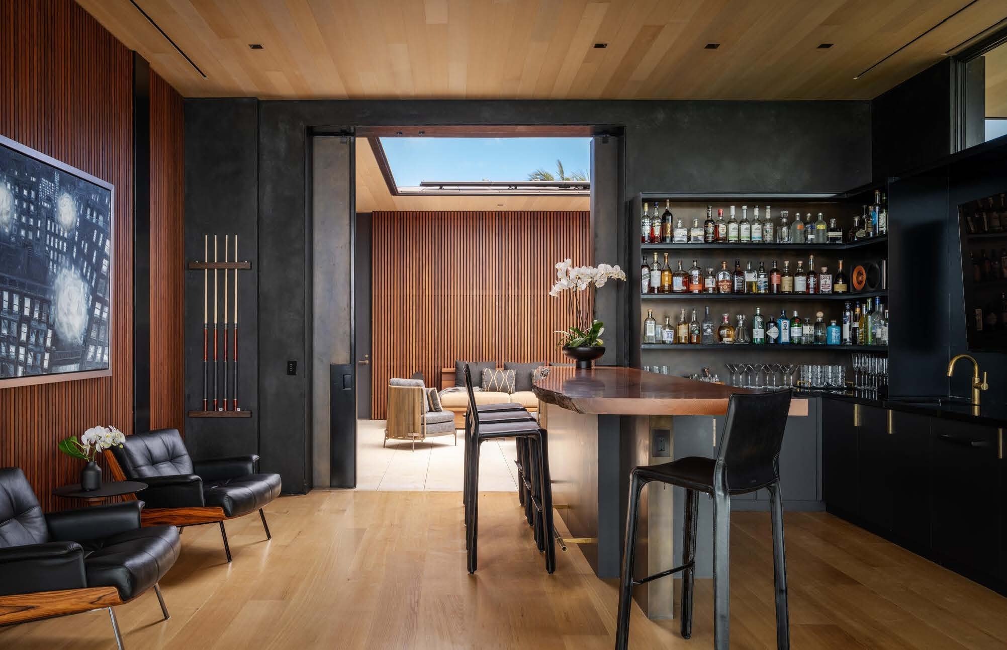 Modern living space with a glass door leading to a patio, a fully stocked bar, and seating area with chairs and a sofa