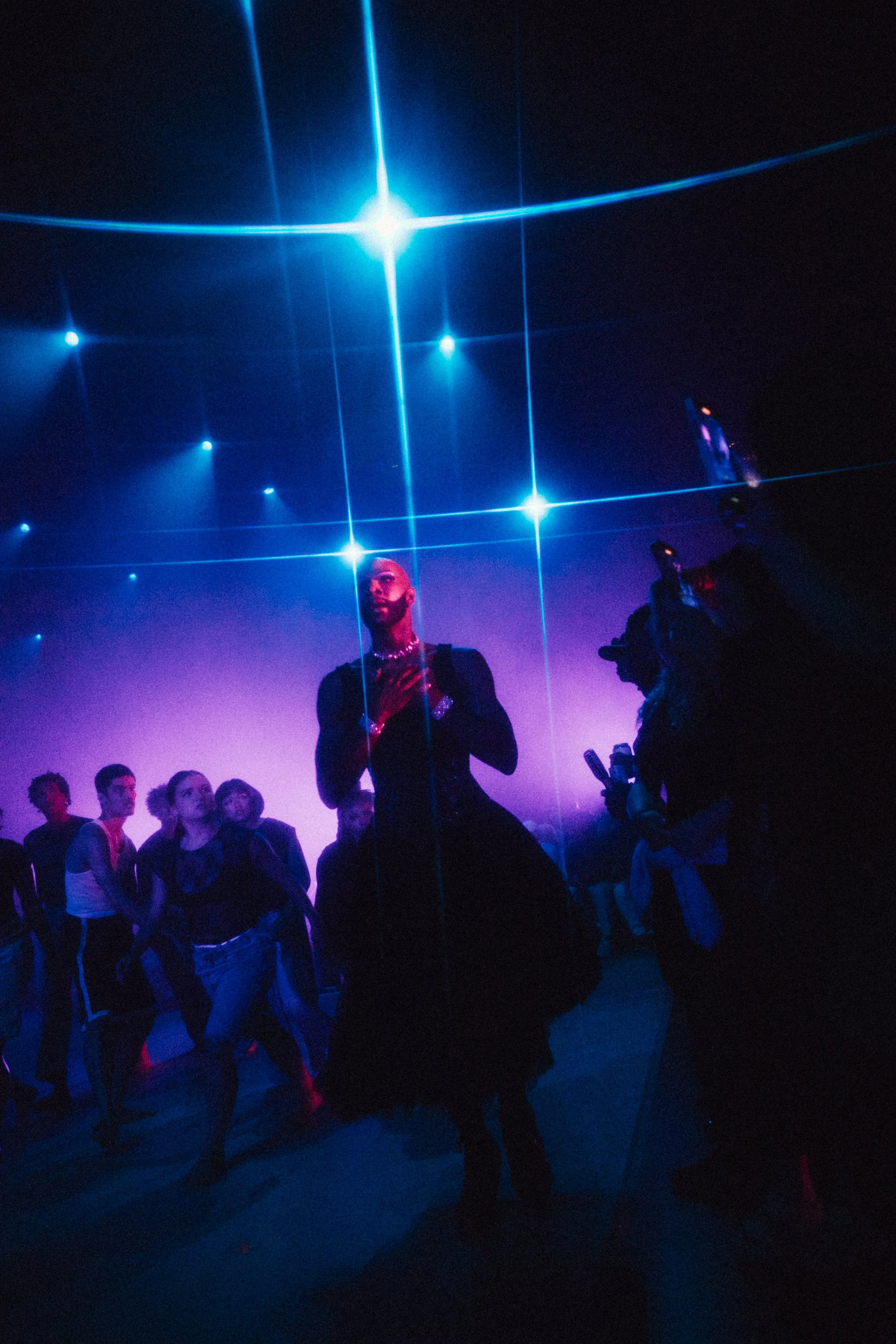 Person dancing Under Blue Spotlights with a group of people in a dark club or party setting.