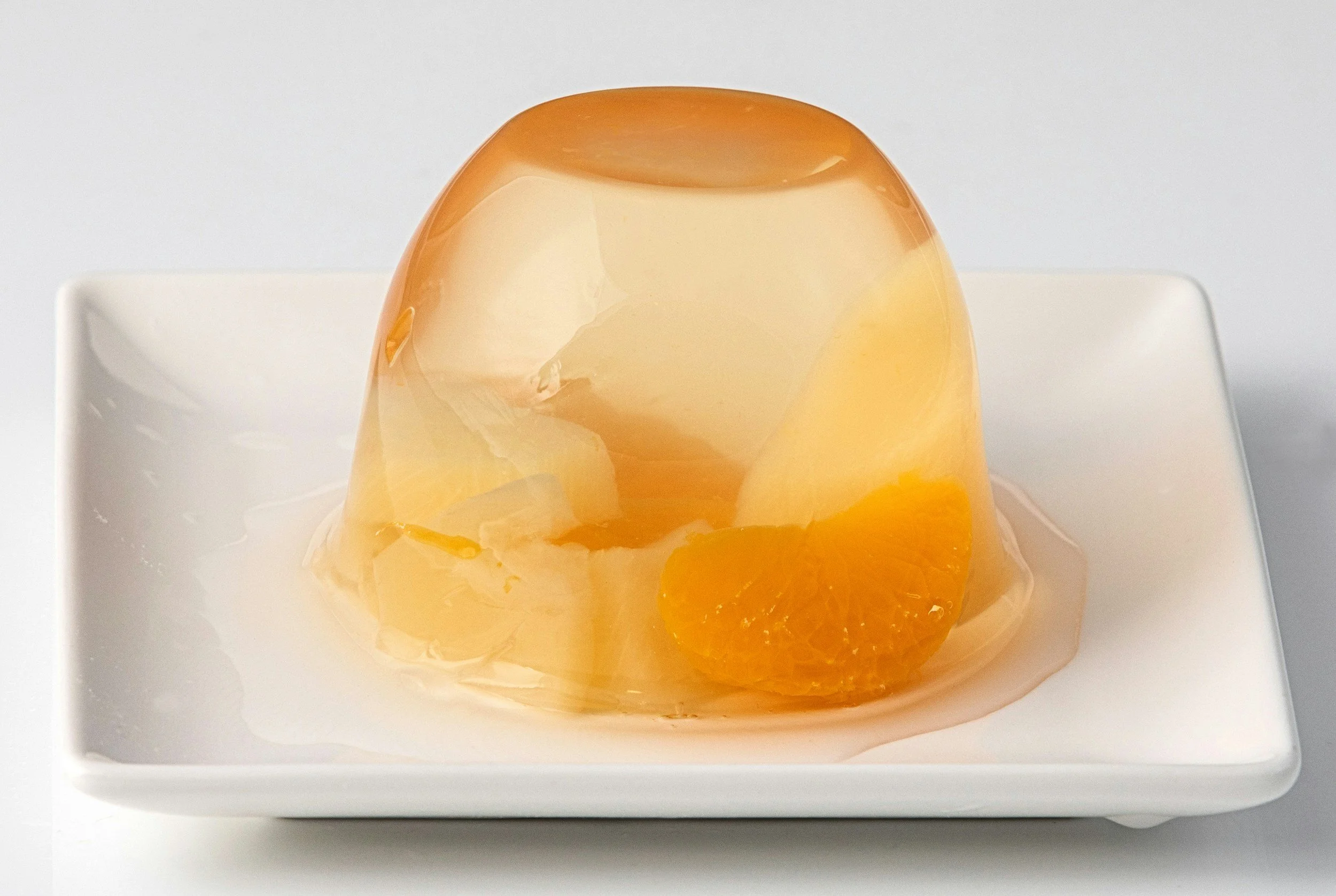A gelatin dessert topped with fruit slices on a white square plate.