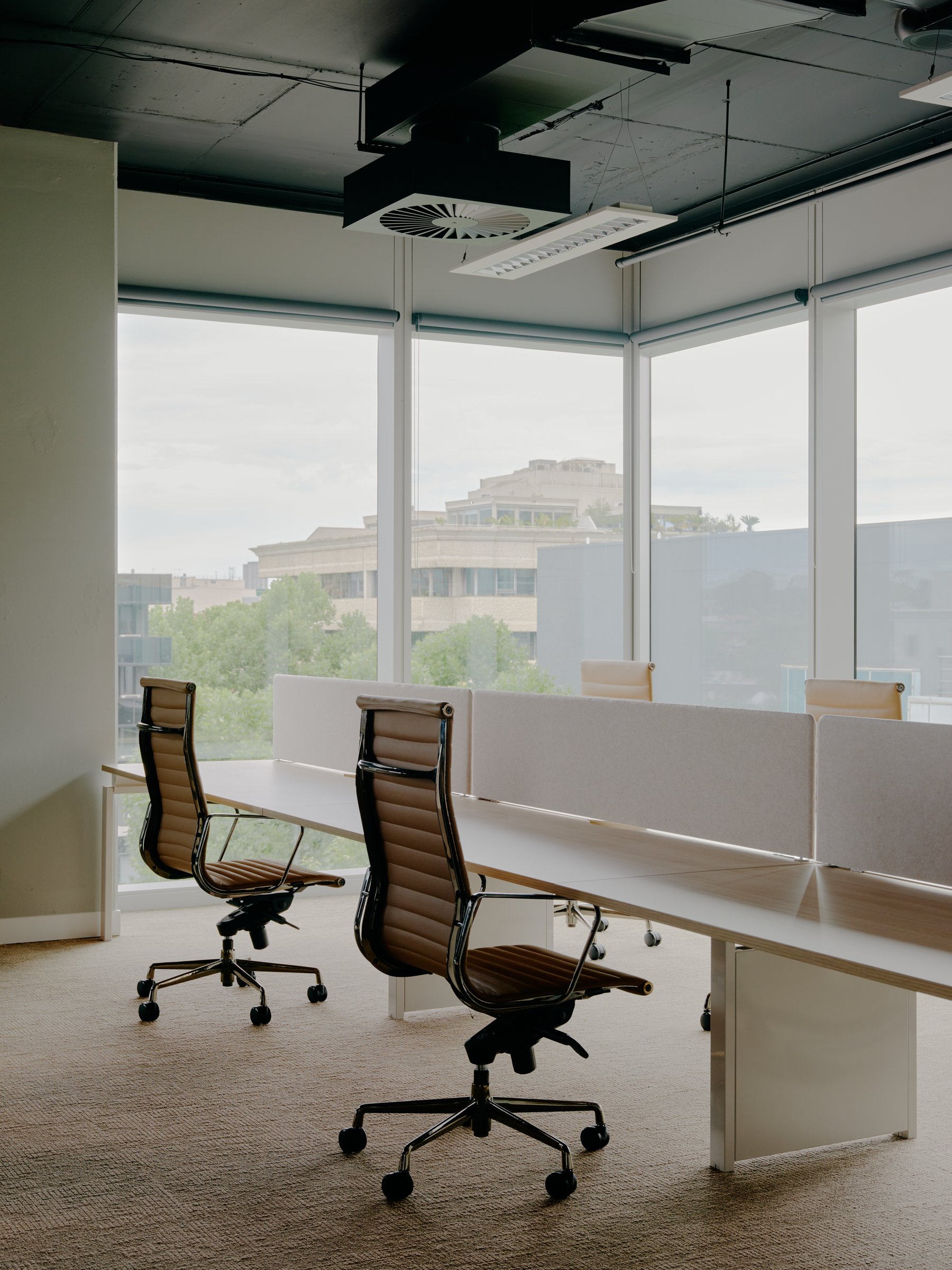 Empty modern office meeting room with glass windows, beige chairs, and a long table.
